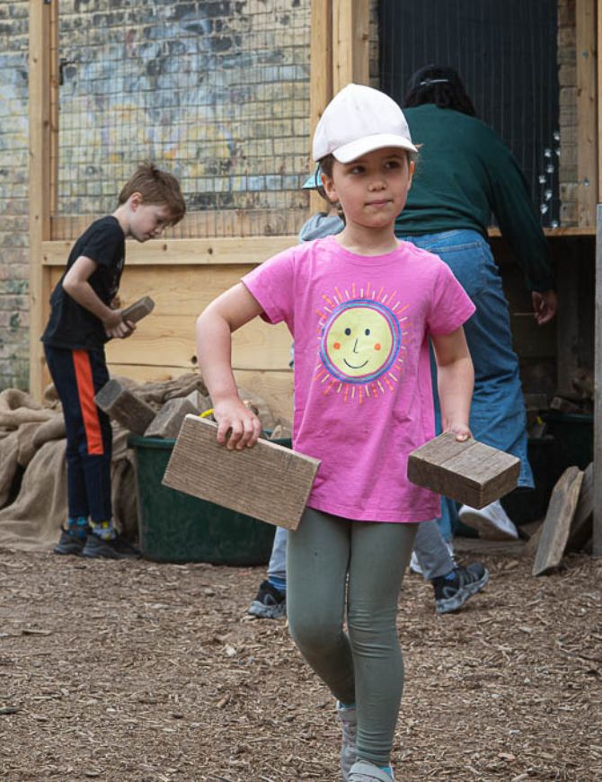 Young girl carrying some blocks of wood at an outdoor play place