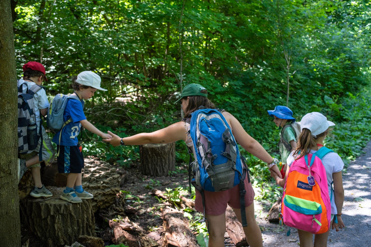 Woman helping children off a tree stump on a walk in the forest.
