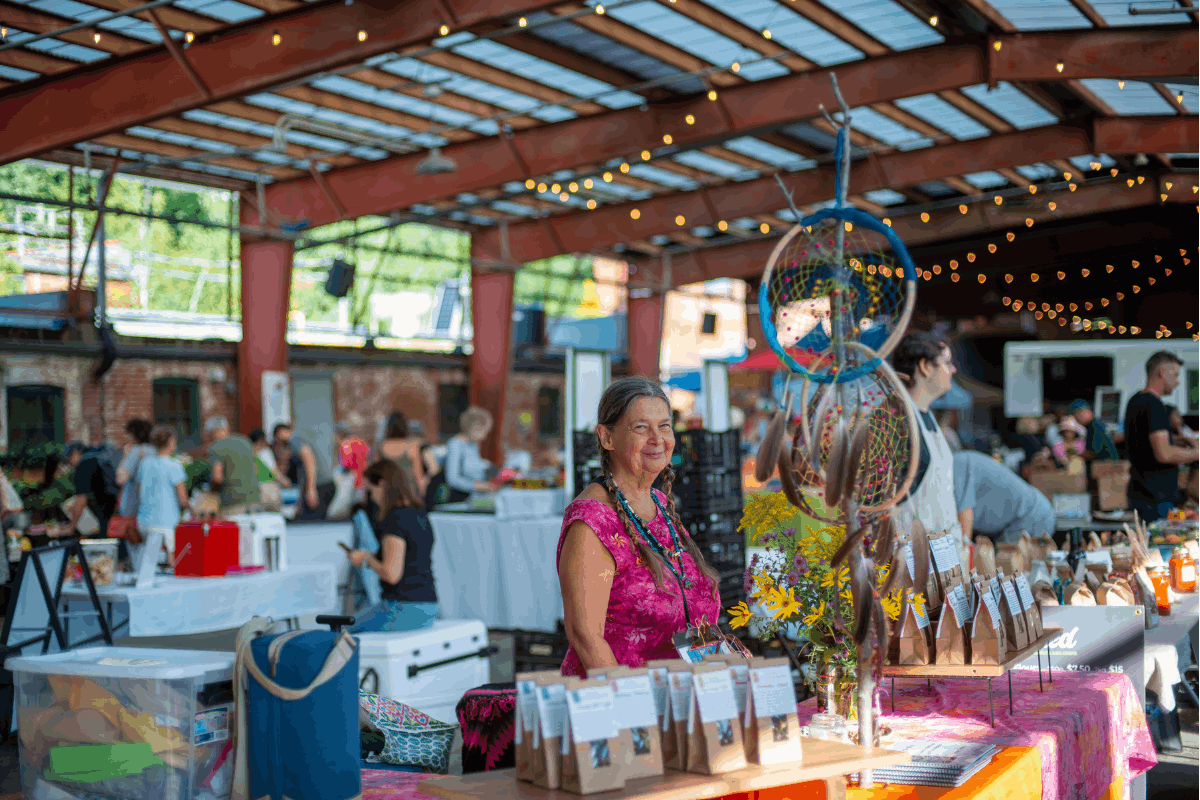 Woman stands in front of her products at the outdoor Saturday Farmers Market