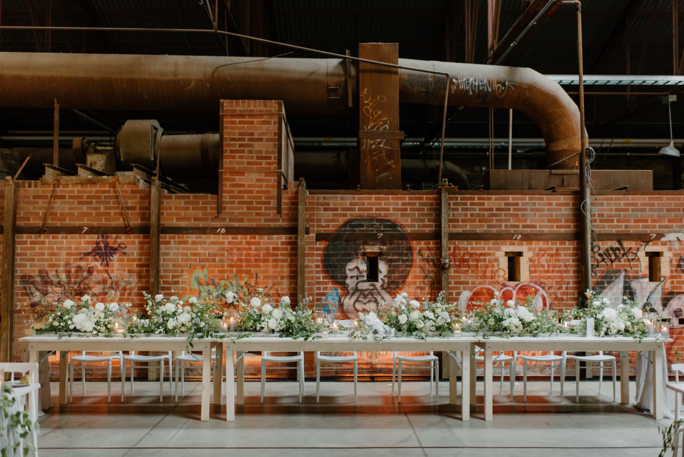 Evergreen Brick Works CRH event space, 3 long white wedding tables with white florals and exposed brick kilns backdrop.
