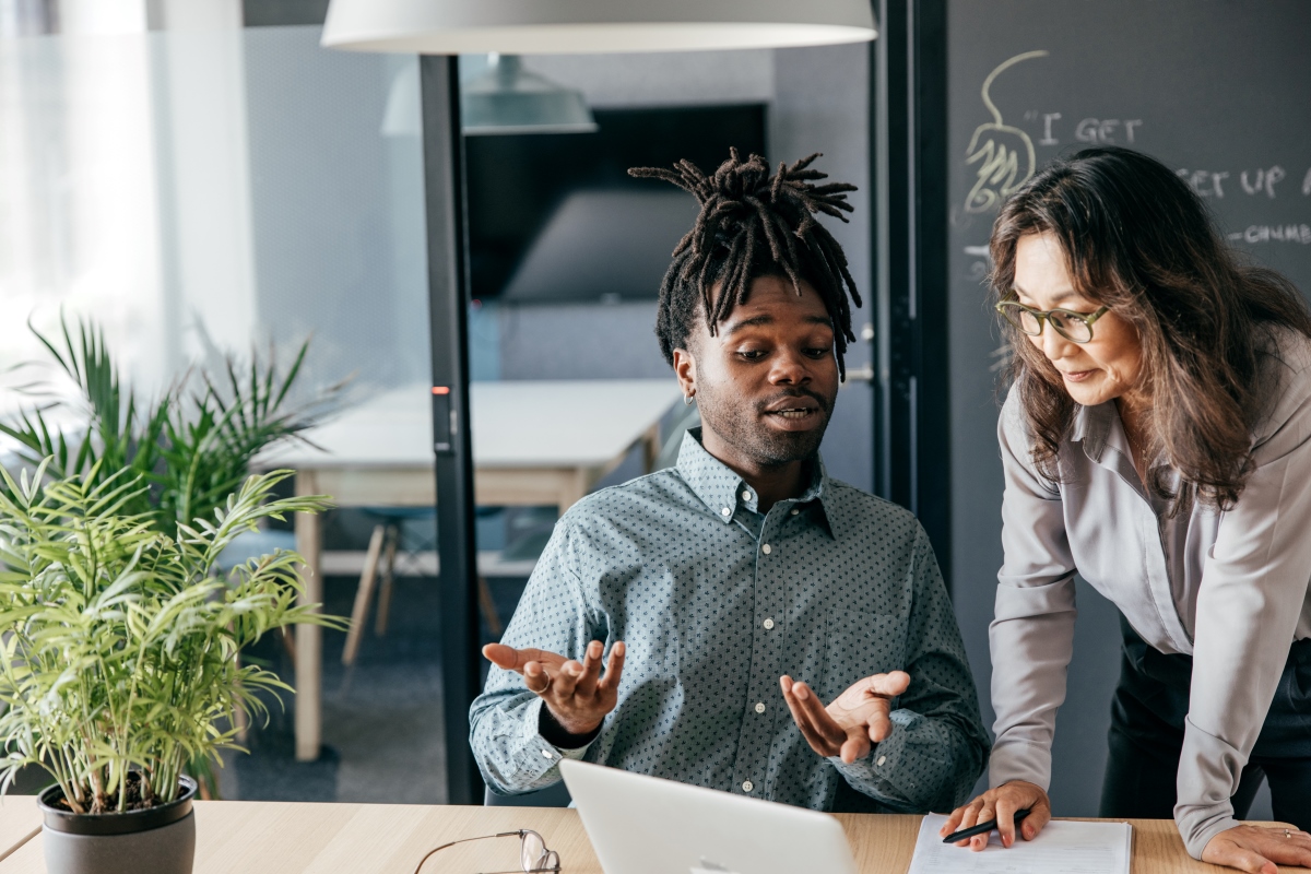 Man sitting and talking with woman looking at his computer in an office