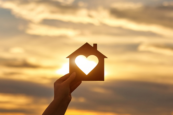 woman-hand-holds-wooden-house-in-the-form-of-heart-against-the-sun