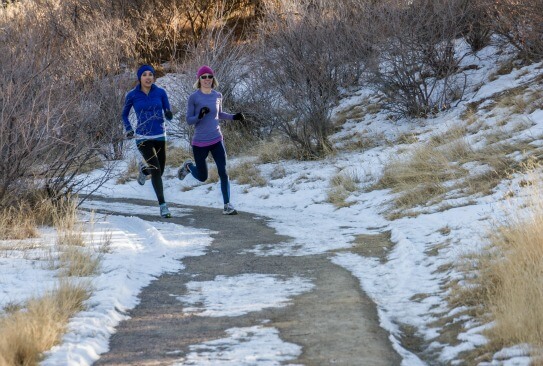 Evergreen Brick Works trail covered in snow with two individuals running.