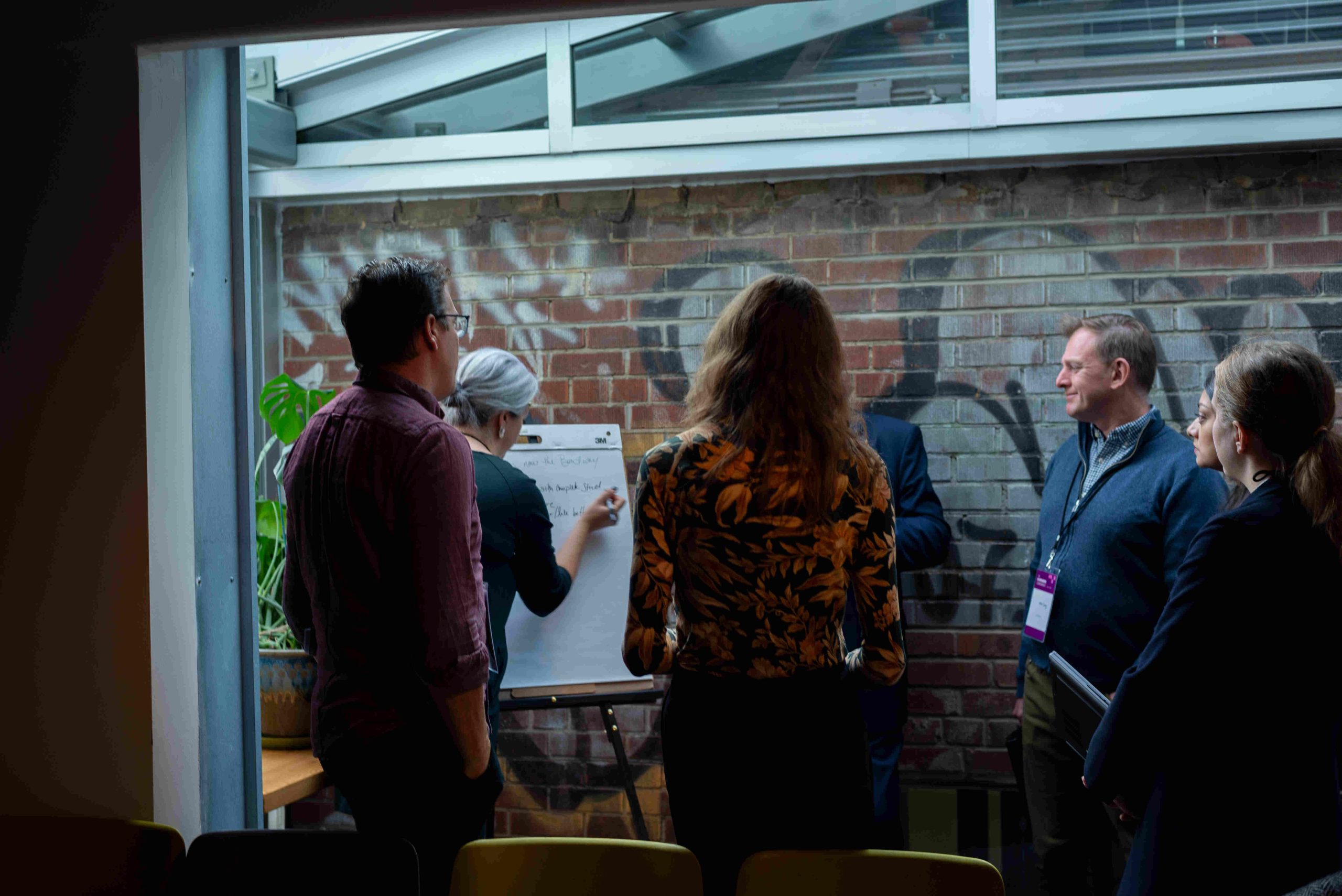 Group of people stand around a notepad in a meeting room