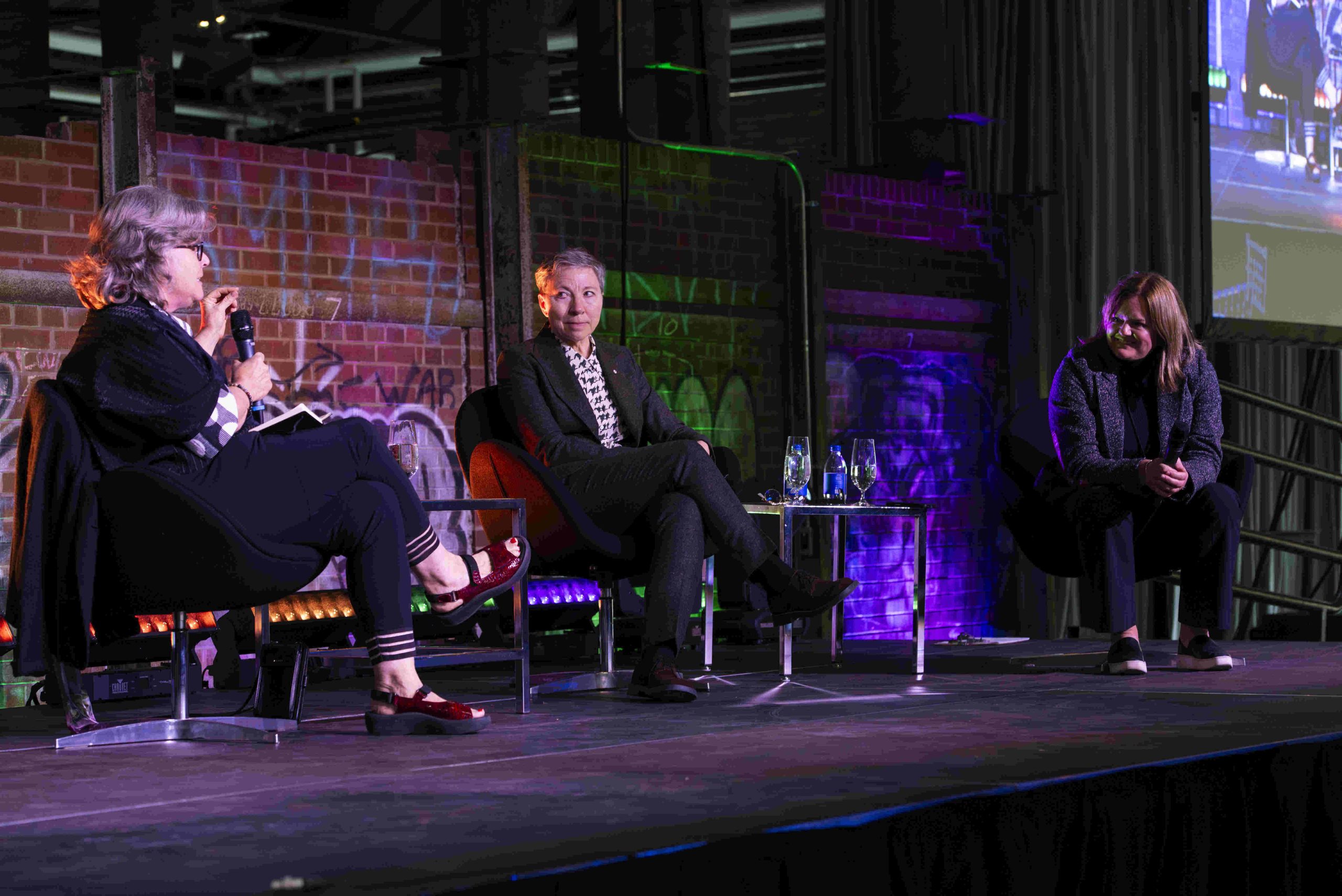 Panel discussion group of three sit on stage
