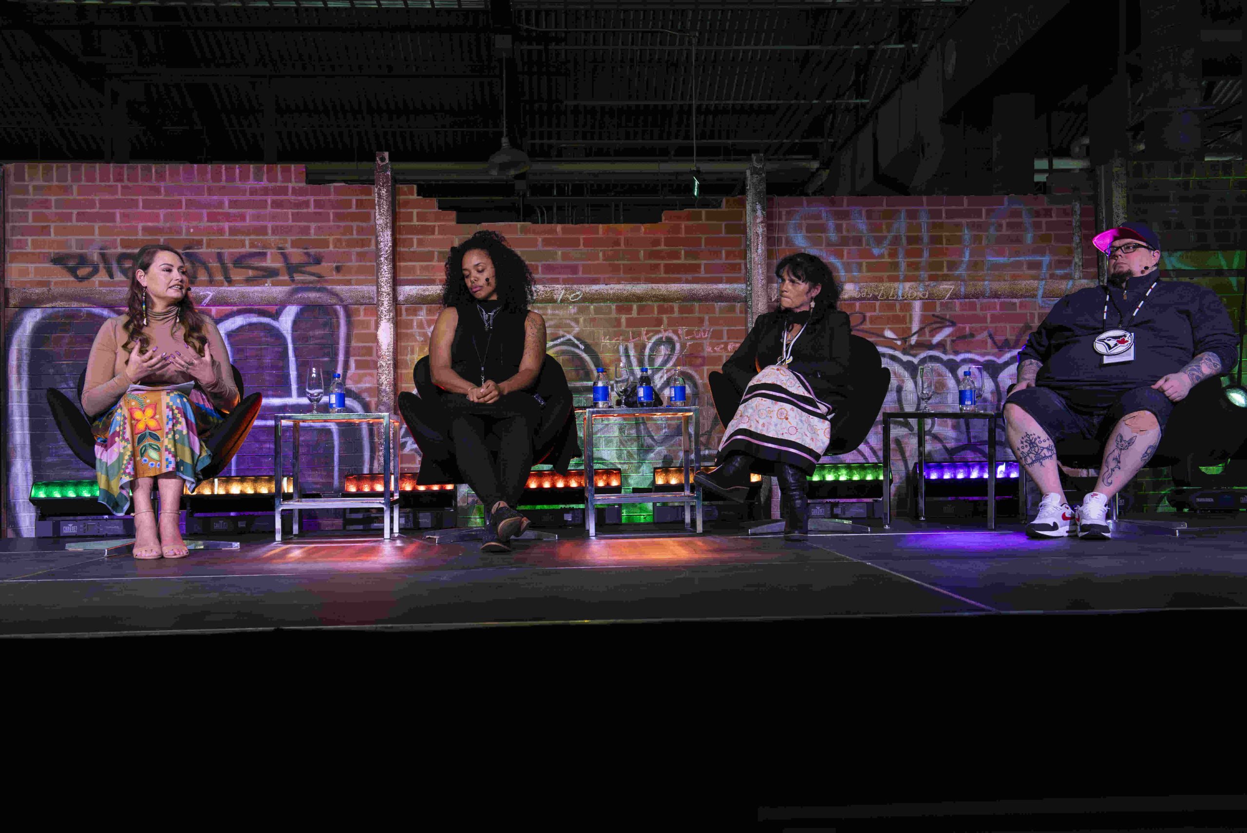 Panel discussion group of 4 panelists sit on chairs on stage