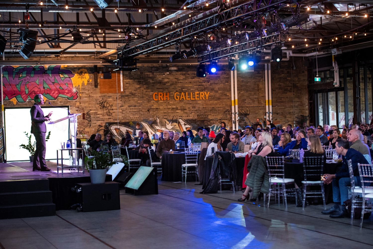 Group of people sitting at tables at conference listening to speaker on stage