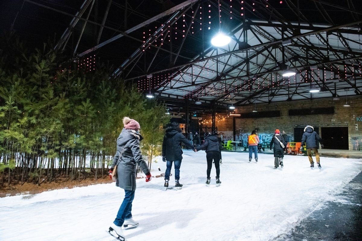 People ice skating on trail at night with brick building in background