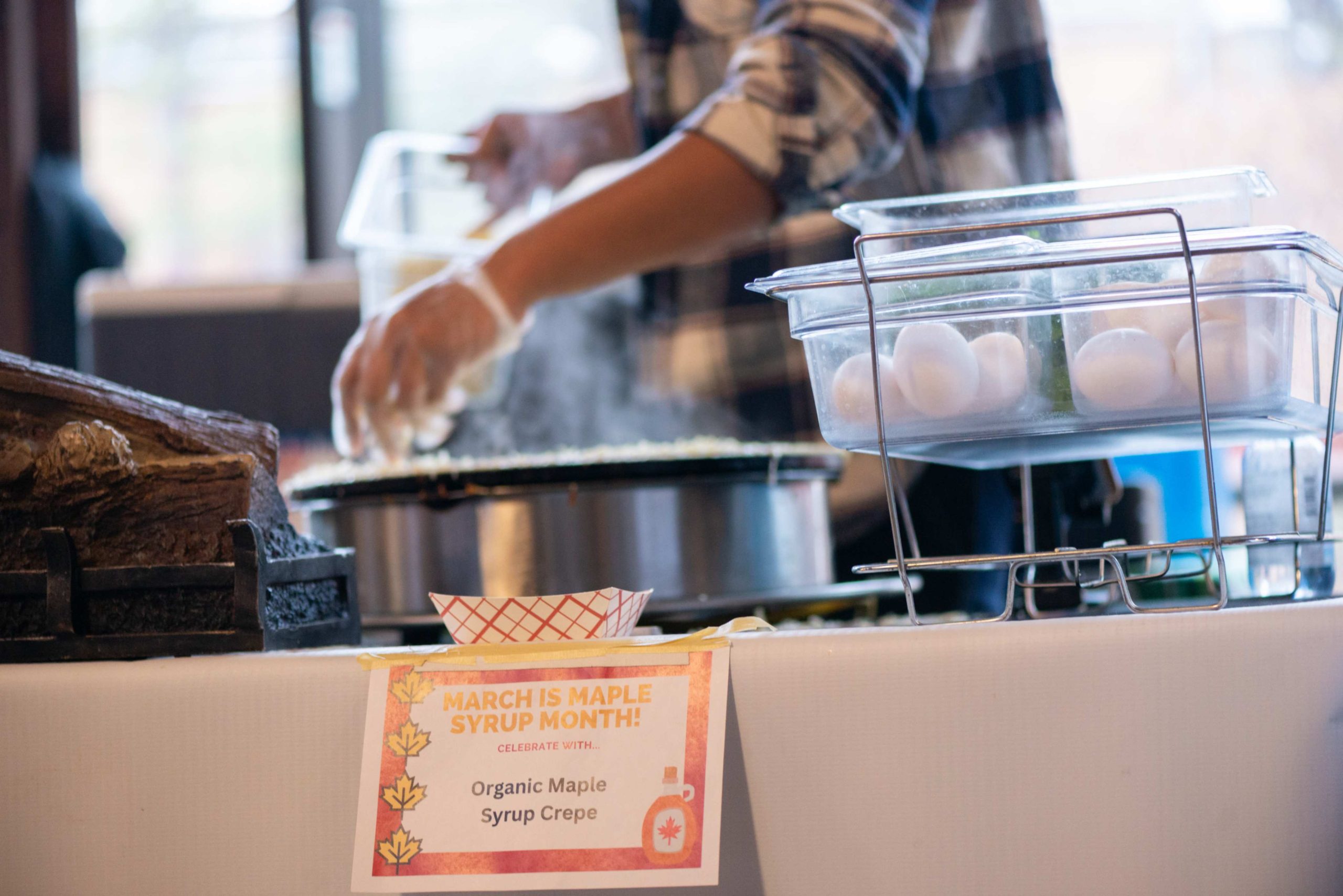 Person making crepes at the Farmers Market with a sign promoting Maple Syrup Month