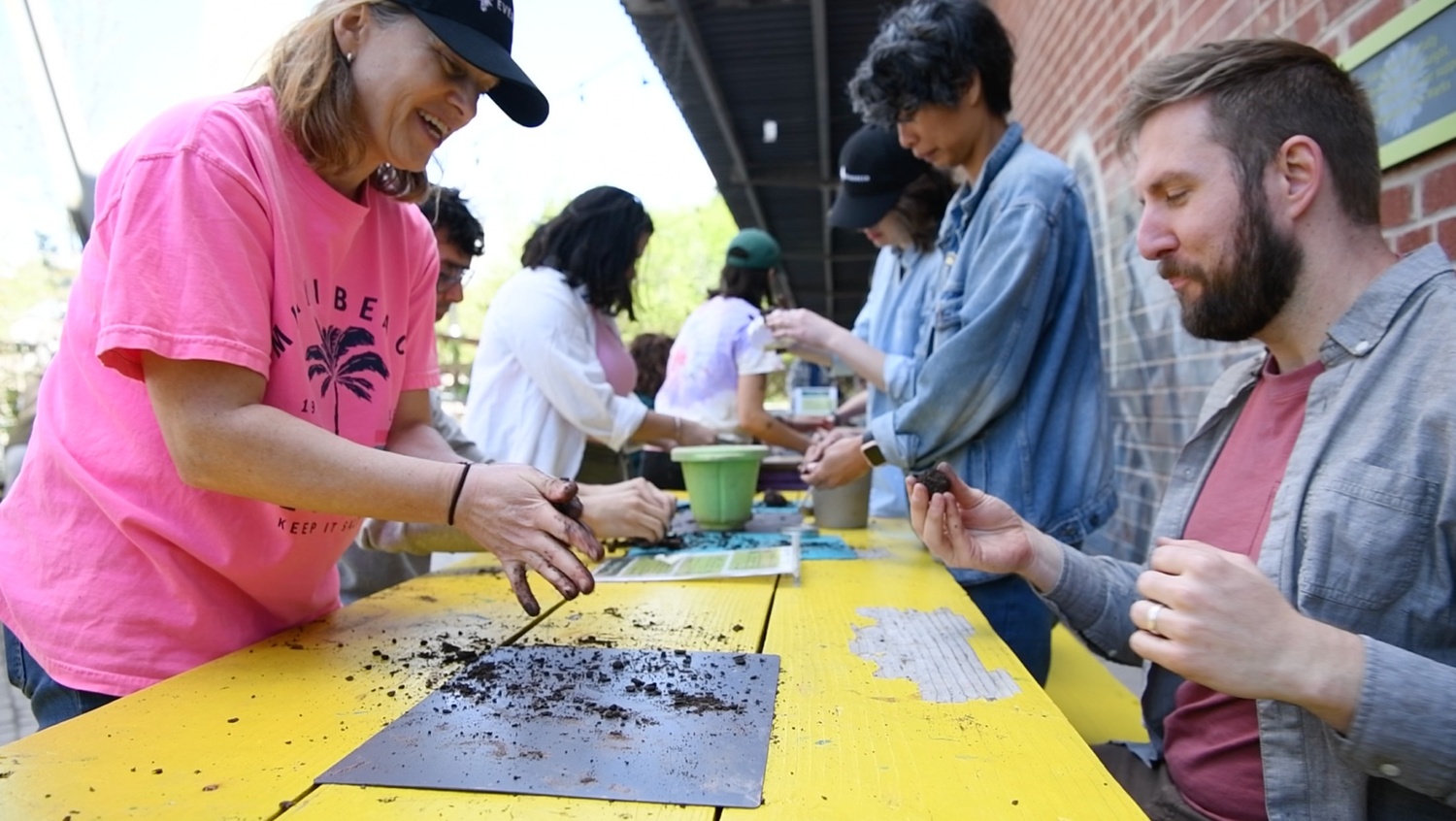 A group of people sit at colourful picnic tables using soil and clay to make seed balls