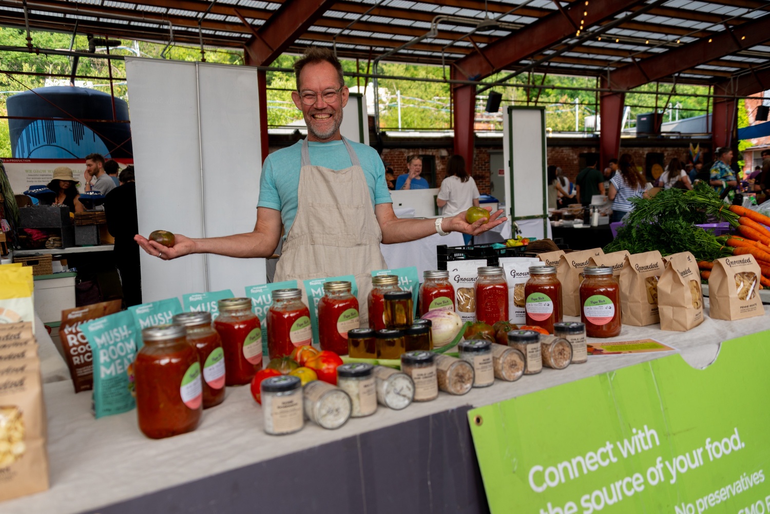 Man stands smiling at a farmers market booth in front of a selection of tomato salsas.