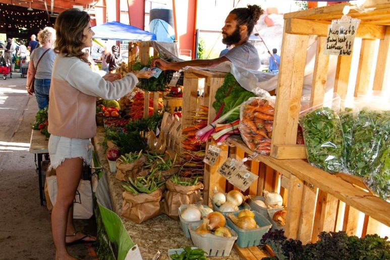 a person is buying veggies at a famers market stall
