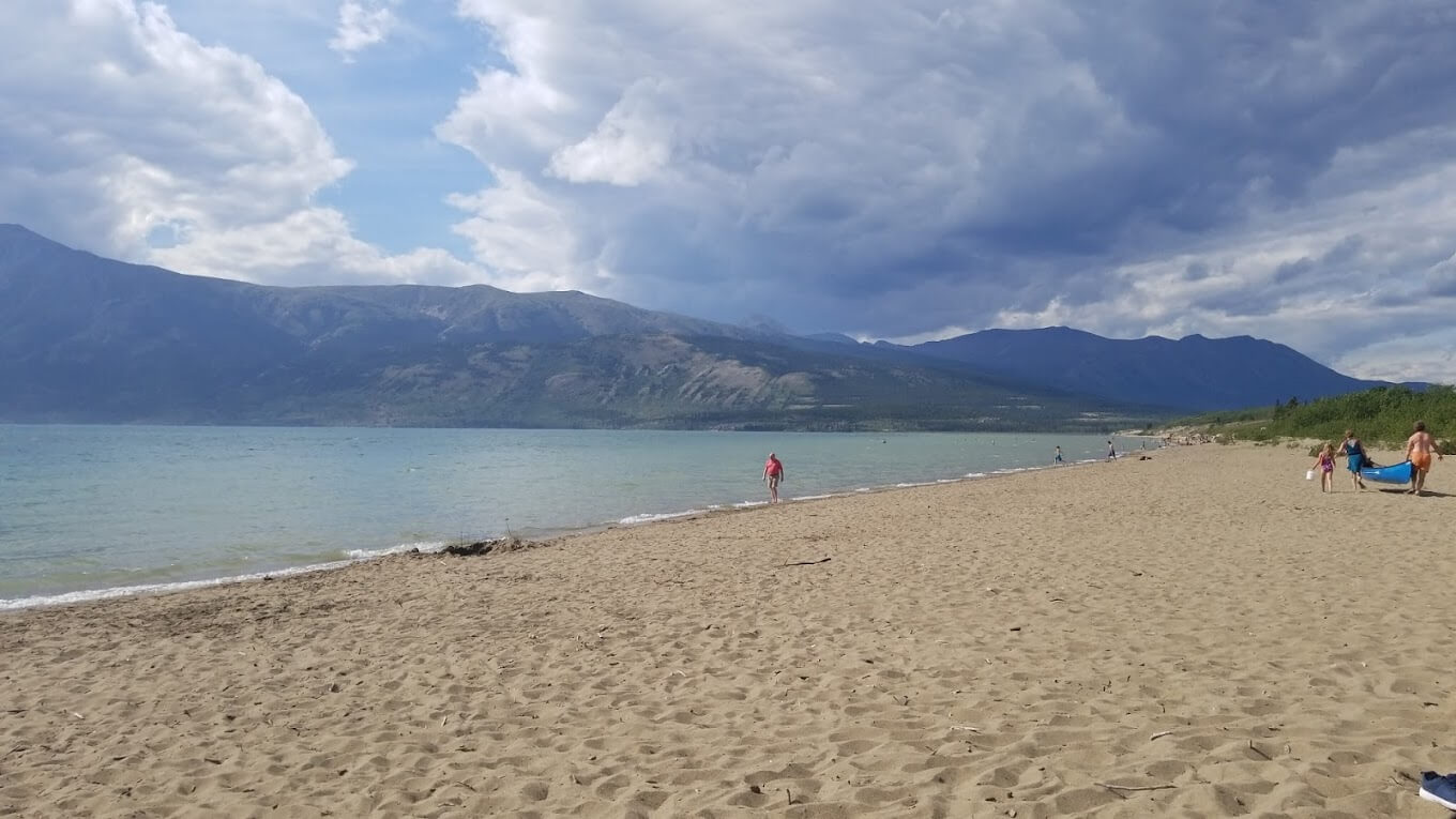 People walk on sand on beach with mountains in background
