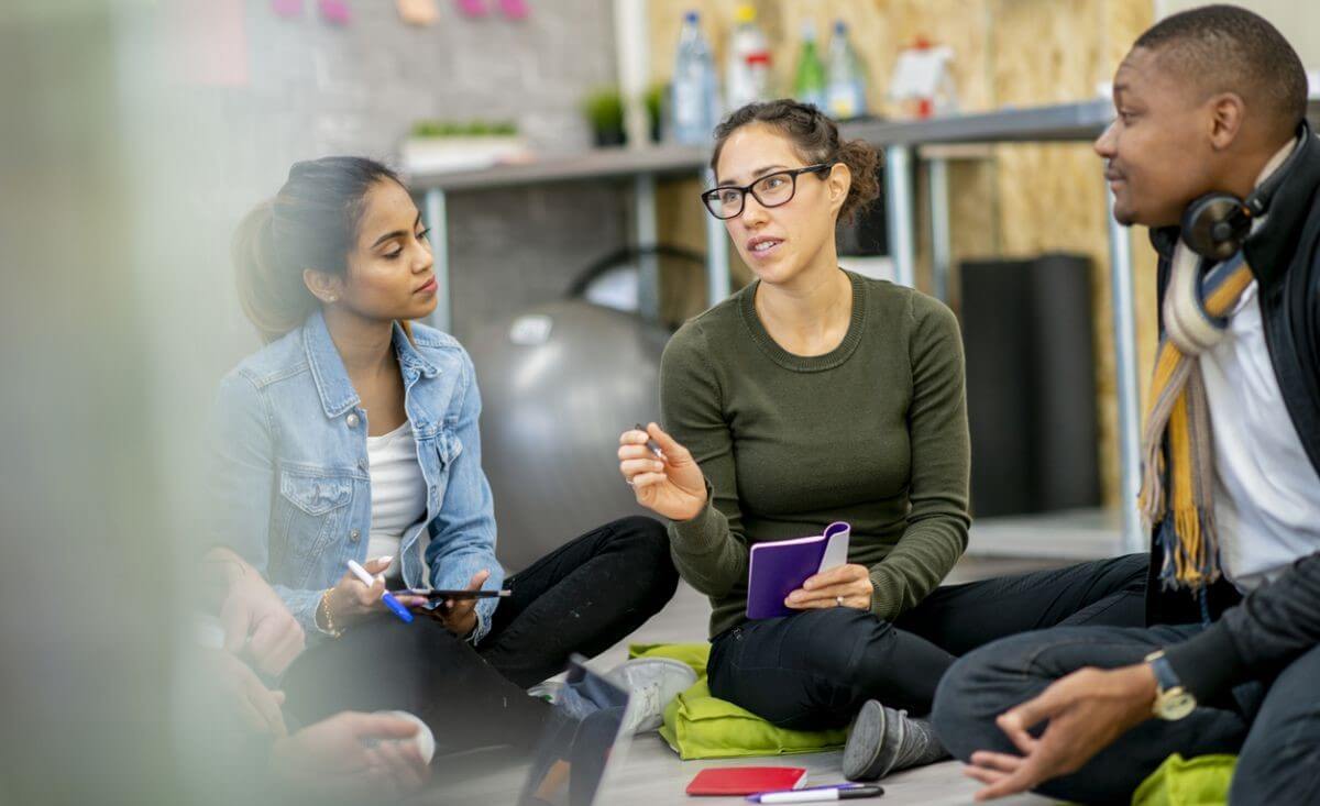 three young people sit on the floor during a brainstorm sessions discussing ideas