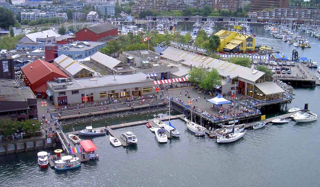 Photo aérienne de Granville island montrant l'eau, des bateaux, des bâtiments et des promenades