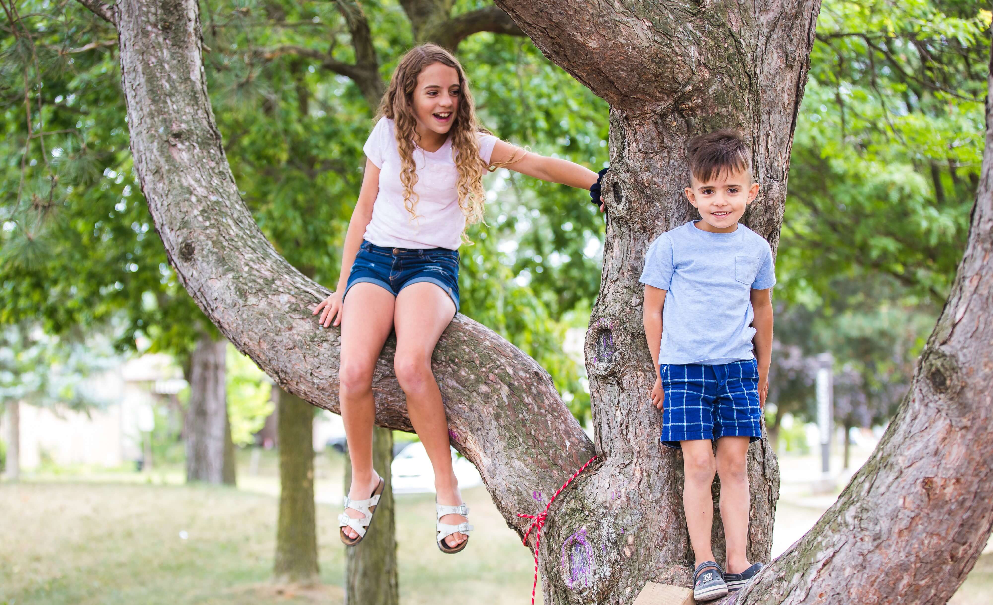 two kids play near and on a tree