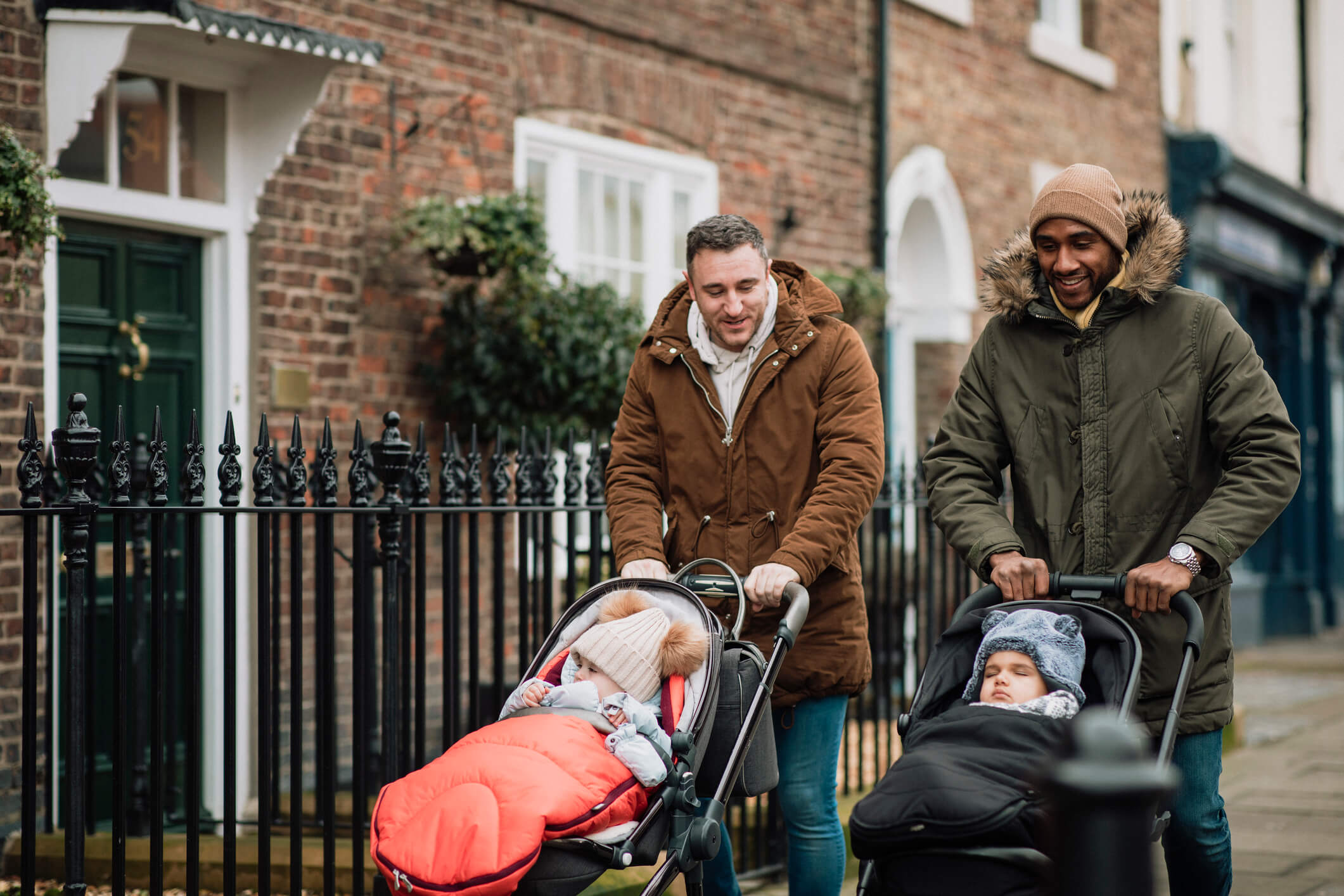 Two men walk along the street with strollers and babies