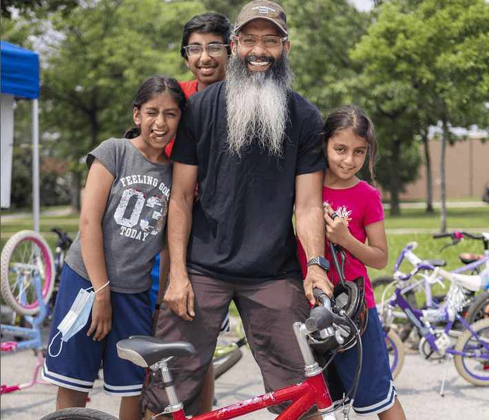 Faysal with three kids standing outdoors behind a bicycle