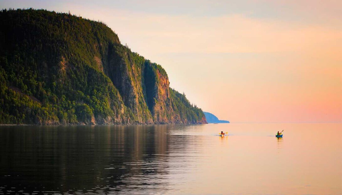 People kayak in water with clifs in the background