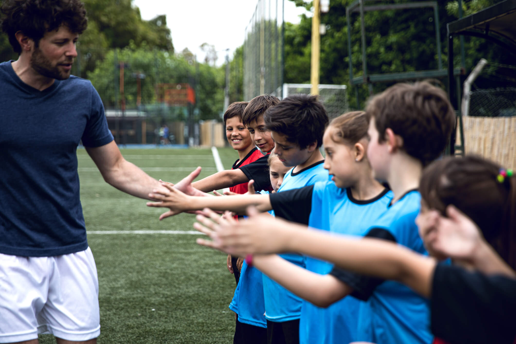 Group of boys and girls high five their coach on a soccer field