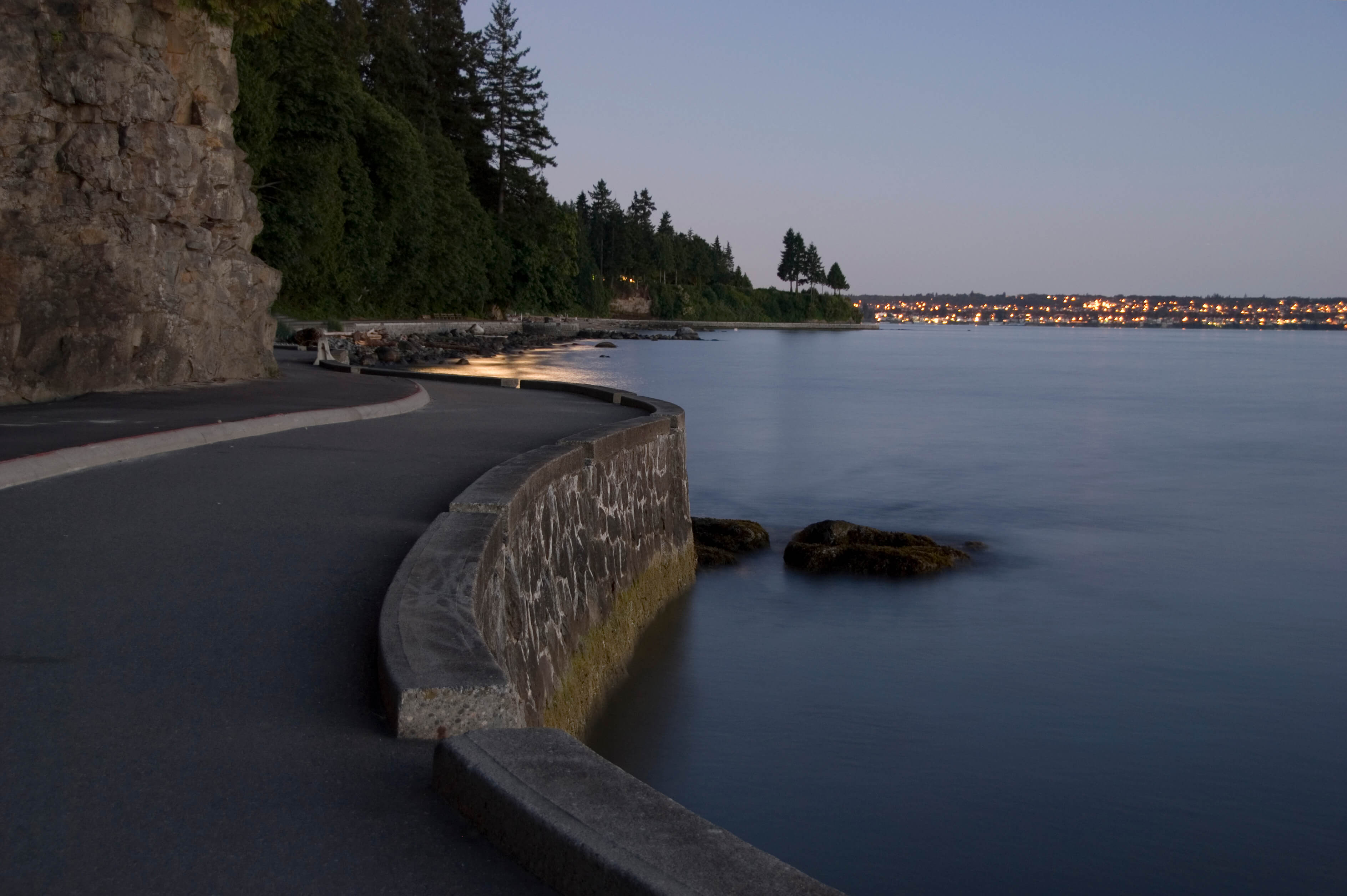 A stretch of paved road running along the waterfront, with Vancouver in the background