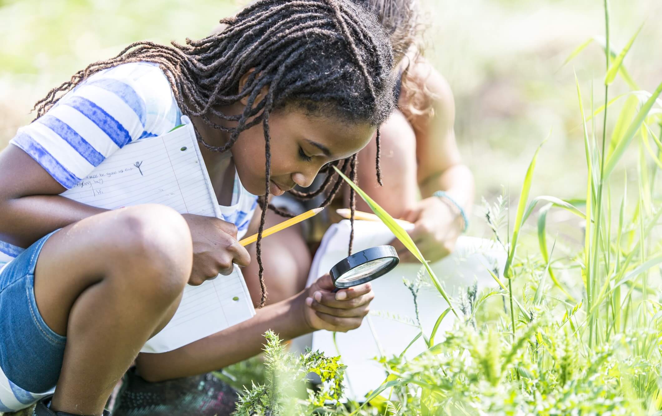 Girl looks at magnifying glass in nature. holds paper and pencil